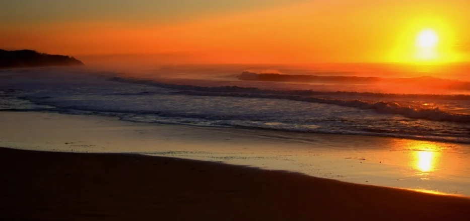 a beach is filled with waves and an orange sunset