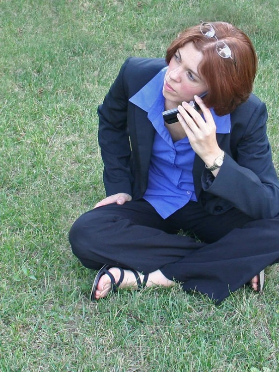 a young woman sitting in the grass talking on her cell phone