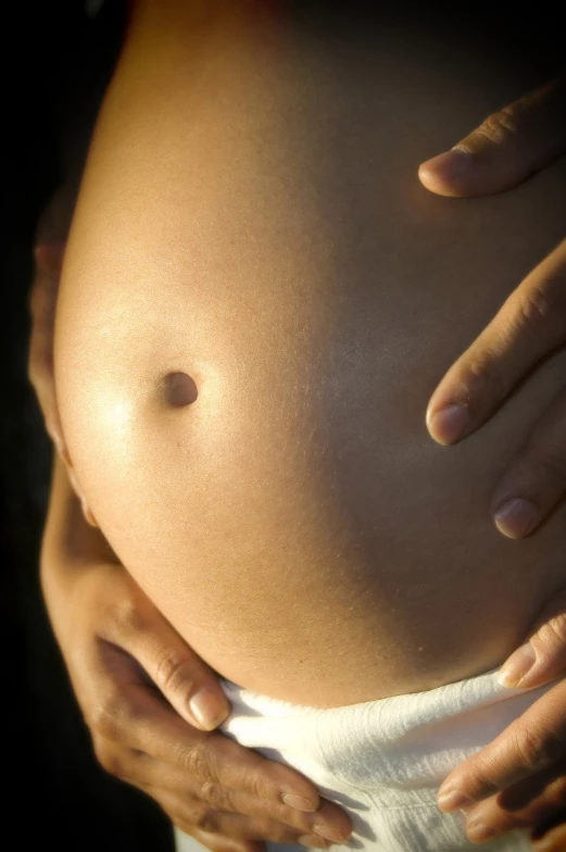 a pregnant woman's belly and hand with light reflecting off it