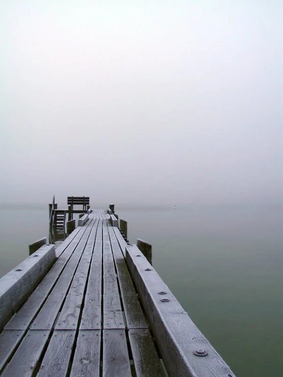 a wooden dock with benches on it in the foggy day