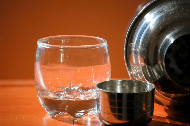 an empty glass of water next to a silver mug on a wooden surface
