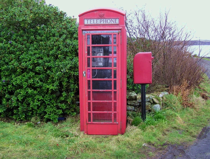 a telephone booth is sitting beside bushes and a street