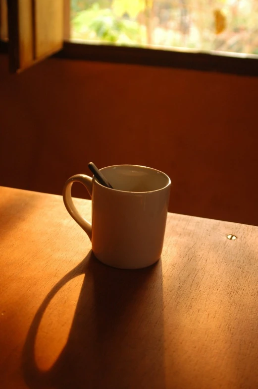 a cup sits on a wooden table near a window