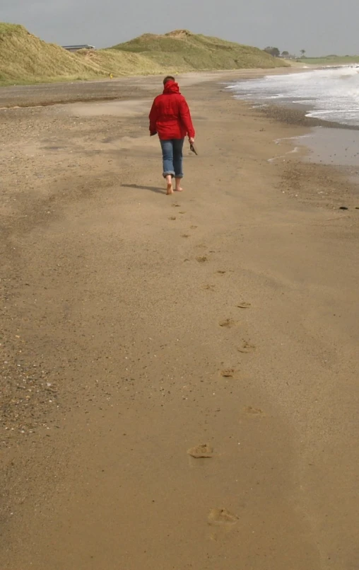 a person wearing a red jacket walking down a beach