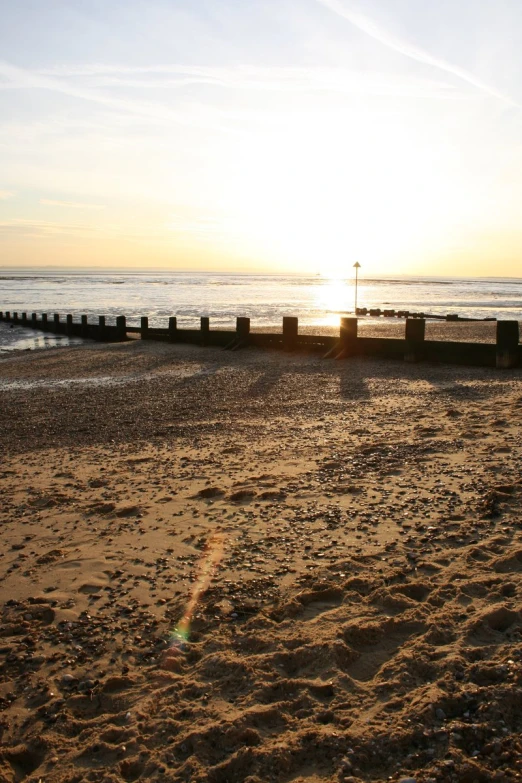 a bench on the beach at sunset with the sun rising