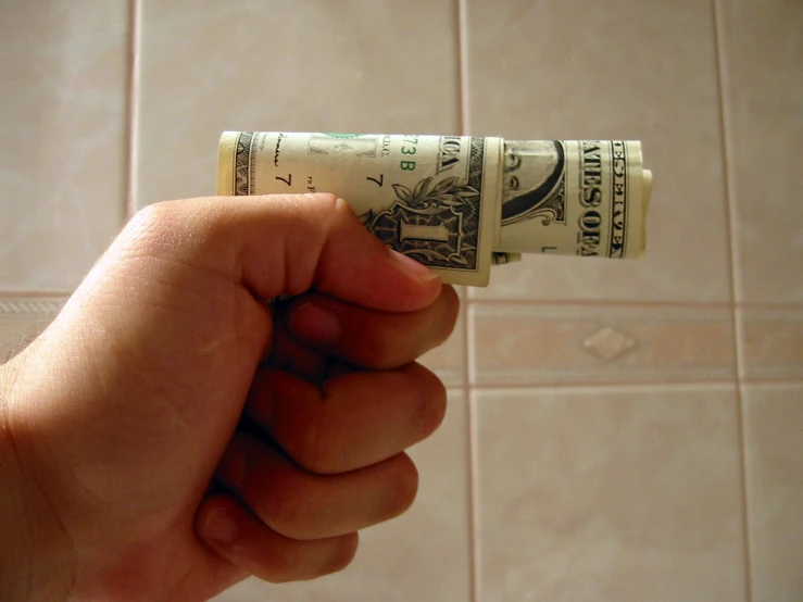 the hand is holding money in front of a bathroom wall