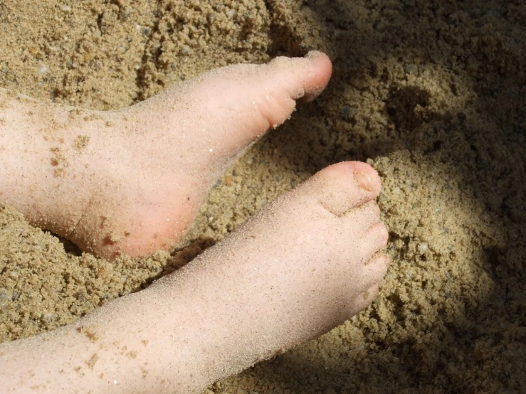 the feet of someone laying in sand on top of a beach