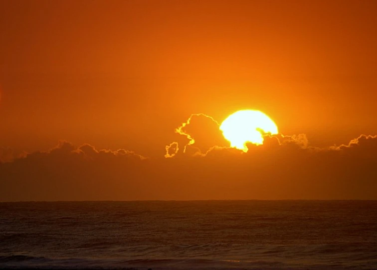 an orange sunset with the sun behind clouds