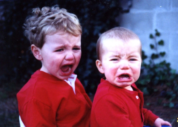 two boys with red shirts are sitting outside