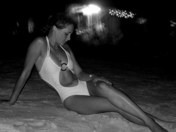 a girl in a white swim suit sits on the sand