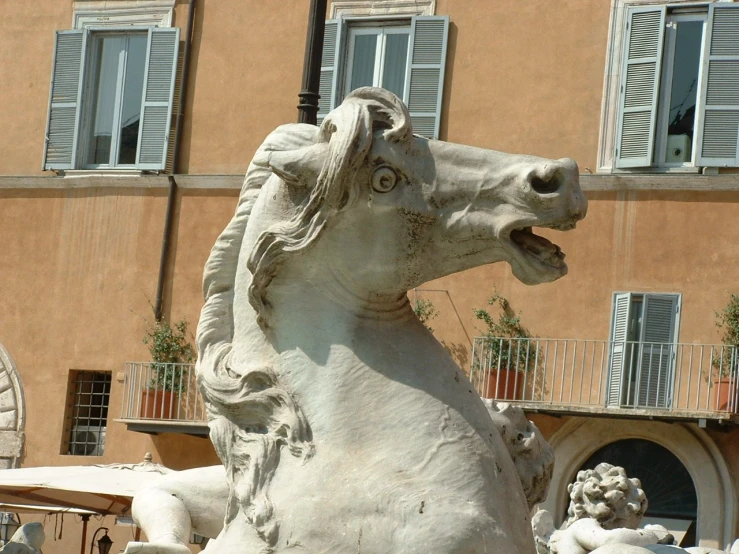 a marble statue of a man riding a horse with a horse mane, holding his hind legs in front of an apartment building