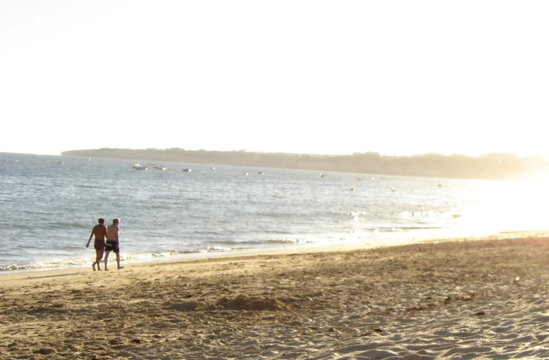 people walk along a beach while the sun shines on the ocean