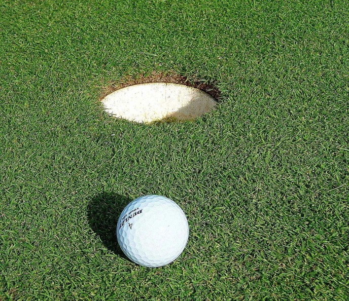 the white ball is near the hole on the golf course