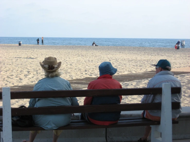 three people sitting on a bench overlooking the beach