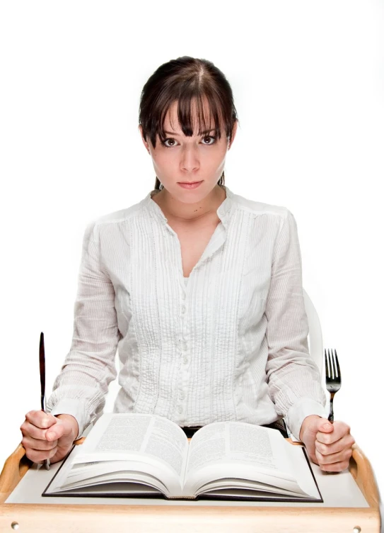 a woman sitting at a table with an open book and fork in front of her