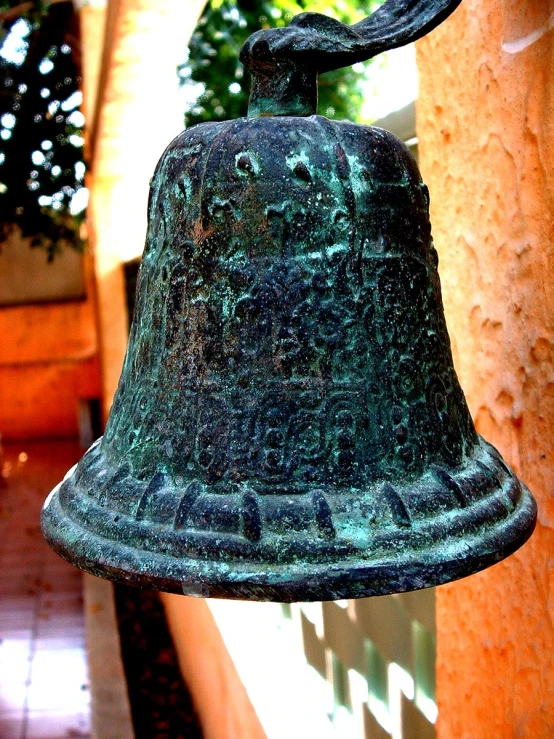a green metal bell hanging from the side of a building