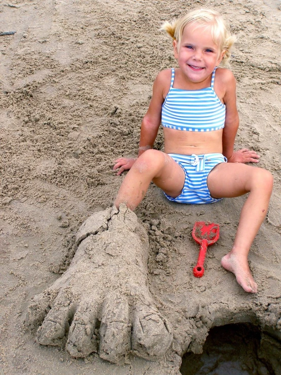 a little girl sits in the sand on the beach