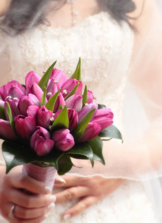 a bride is holding a bouquet of pink tulips