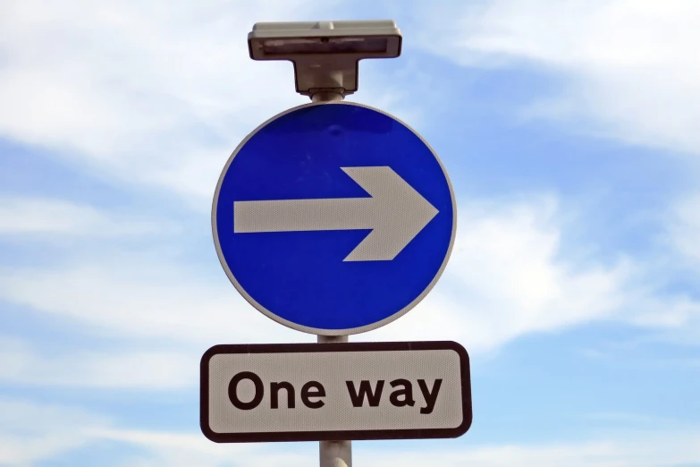 a one way sign under a blue sky with clouds