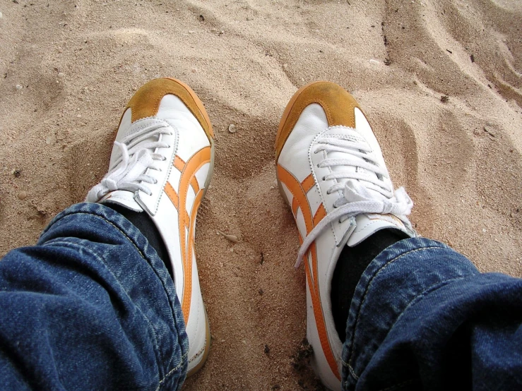 a person standing on top of a sandy beach next to a white and orange shoe