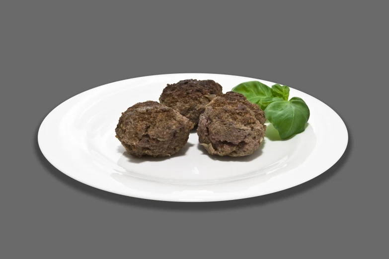 a white plate holding four pieces of meat and a small piece of leaf