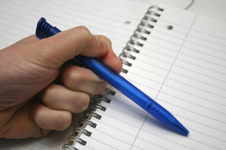 there is a hand that is writing on a spiral notebook