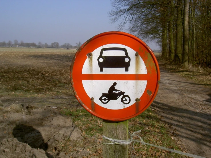 there is a sign on the side of a dirt road with a car and motorcycle