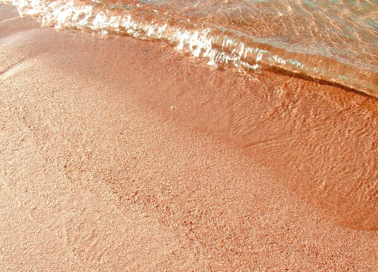 a beach with a red sand area and waves crashing onto it