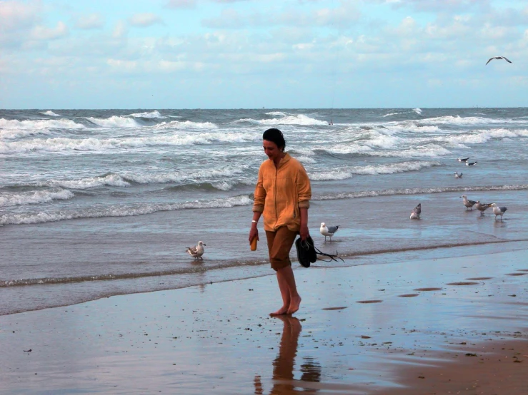 a man in a yellow shirt on the beach looking at some seagulls