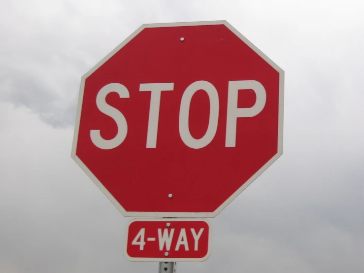a four way stop sign in front of grey sky