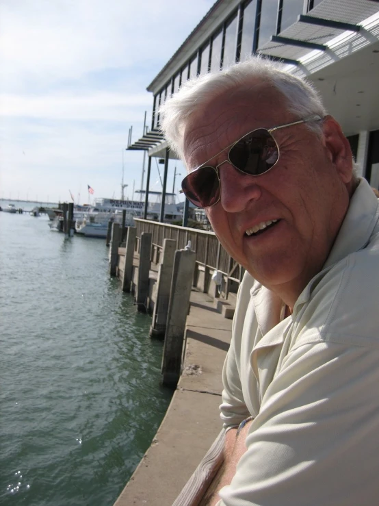 an old man smiles as he sits on a pier