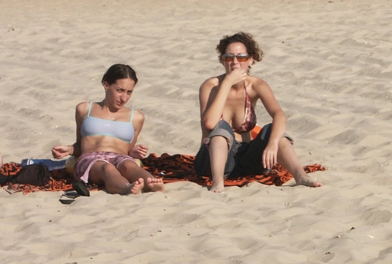 two people sit in the sand on a beach