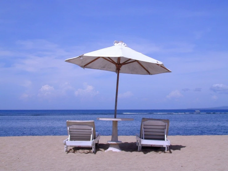 two white chairs sitting under an umbrella on the beach