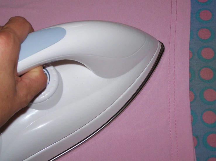 someone's hand is holding an electric iron and it appears to be on the pink bed spread
