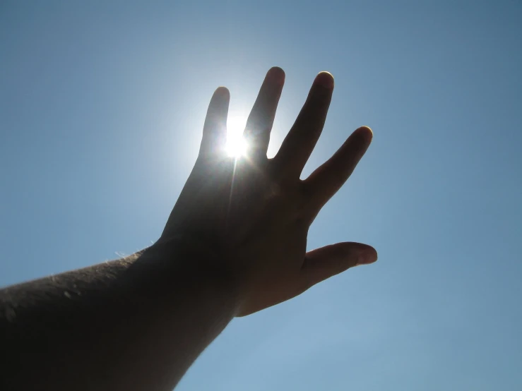 a hand reaching out toward the sky for a bright sun