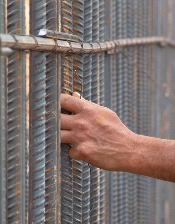 a man's hand reaches out from between a fence and steel gates