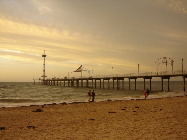 the ocean with a long pier to the right and three people on the sand