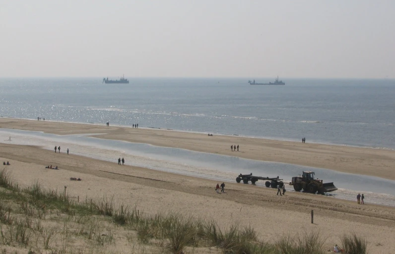 beach scene with people walking on sand near water and ships