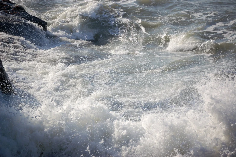 the ocean waves crash next to rocks as a boat sails by