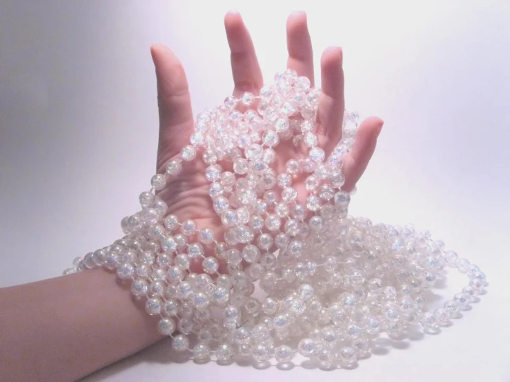 a hand holds several strands of white glass pearls