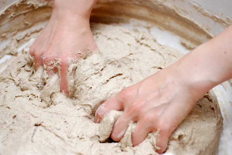 someone kneading bread dough in a white bowl