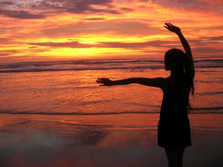 a young woman standing on top of a beach at sunset