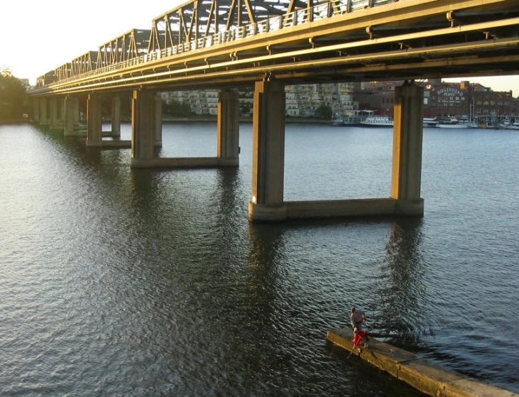 a boat passing under a bridge and water with houses in the distance