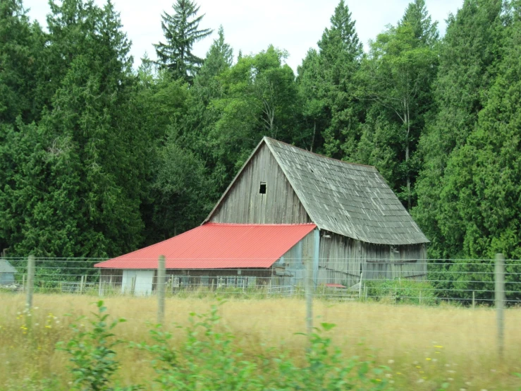 an old barn sits by a forest as seen from the highway