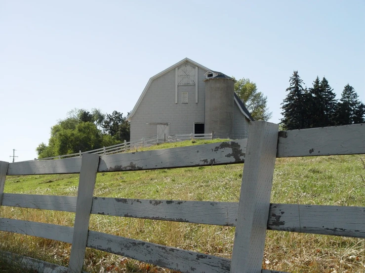 an old barn and a fence in front of a grassy field