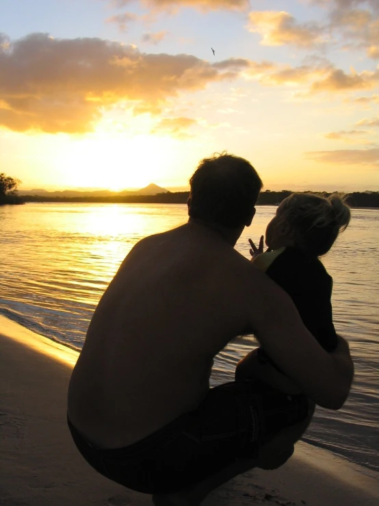 a man and woman sit on the beach at sunset