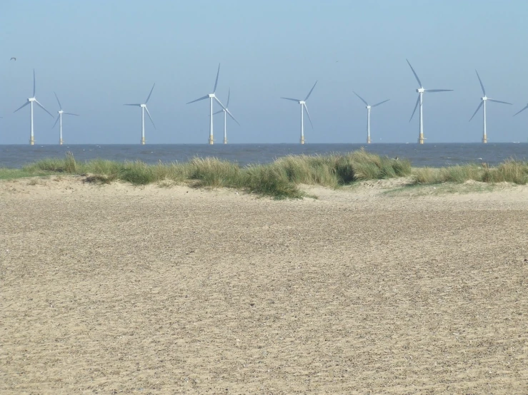 some wind turbines in the distance over water and sand