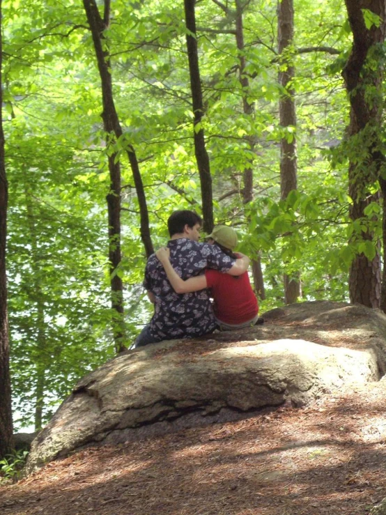 two people in the woods sitting on a rock