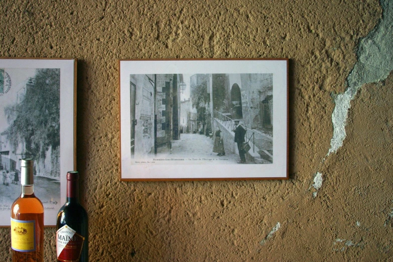 two pictures hang on a wall above two bottles