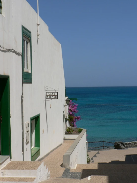 a white building has blue water and purple flowers